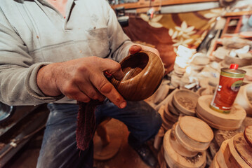 A senior man sitstingin the workshop and smearsing wooden utensils with linseed oil