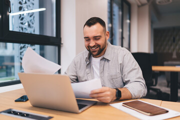 Smiling businessman having paperwork while using computer