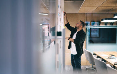 Focused man writing on glass board in office