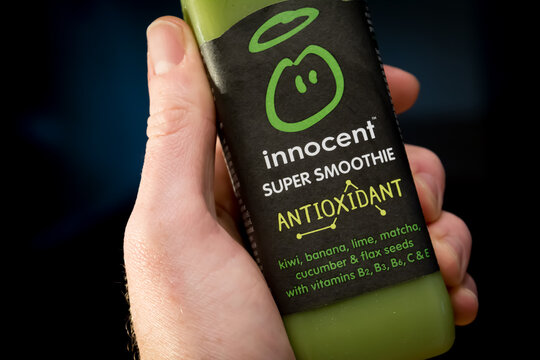 Hand holding green Innocent antioxidant smoothie with kiwi, banana, lime, matcha, cucumber and flax seeds.