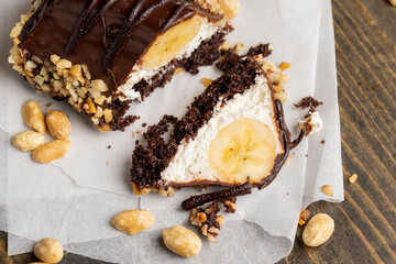 Sliced sweet cake with banana, chocolate glaze, milk filling and peanuts