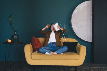 Naklejka premium Woman scattering popcorn while sitting on sofa