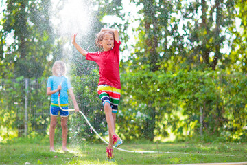 Kids play with water sprinkle hose. Summer garden