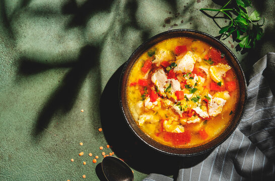 Warming autumn soup with red lentils, chicken fillet, vegetables, spices and paprika, comfort food. Green table, hard light with leaf shadows, top view