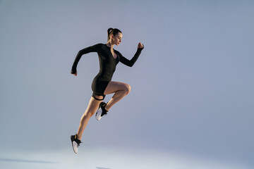 Athletic active woman wearing sportswear jumping on studio background. Dynamic movement