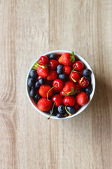 Bowl filled with fresh blueberries, cherries and strawberries on wooden table. Top view.