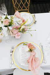 Table service. Close up a plate decorated with pink flowers, a folded napkin and a restaurant menu. The concept of wedding decoration