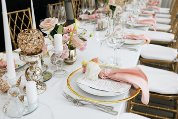 Wedding decorations. Served wedding table with decorative fresh pink flowers and candles. Celebration details. Flower composition roses plates and candles in candlesticks