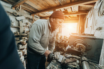 A senior man procesing wood on a lathe and making wooden dishes in the workshop