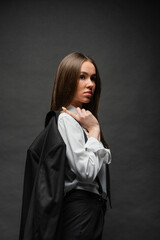 brunette woman with long hair standing in formal wear and holding blazer on black.