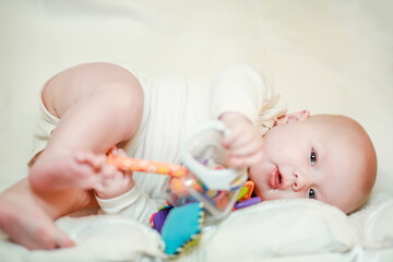 A newborn baby lies on her side and holds an educational toy in her hands. Toy for tactile sensations and the study of shapes and colors of toddlers
