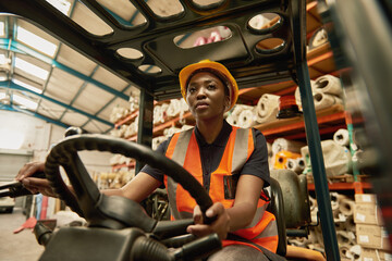 Fototapeta na wymiar Young African female forklift operator driving around a warehouse