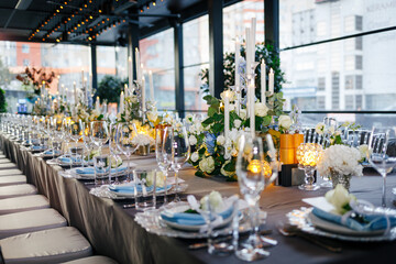 Table setting decorated with a gray tablecloth, silver plates, blue napkins and compositions of white, blue flowers and candles. Concept of wedding decorations 