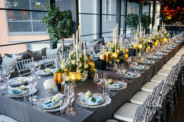Table setting decorated with a gray tablecloth, silver plates, blue napkins and compositions of white, blue flowers and candles. Concept of wedding decorations 