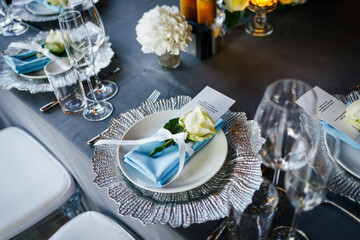 Close-up of a festive table setting. Silver plate decorated with a blue napkin and white natural roses on a gray tablecloth. Wedding decoration concept