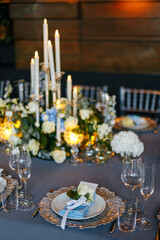 Close-up of a festive table setting. Silver plate decorated with a blue napkin and white natural roses on a gray tablecloth. Wedding decoration concept 