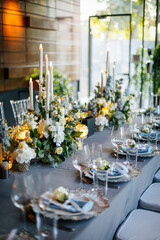 Table setting decorated with a gray tablecloth, silver plates, blue napkins and compositions of white, blue flowers and candles. Concept of wedding decorations 