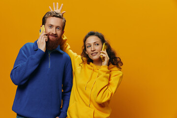 Woman and man cheerful couple with phones in hand talking on cell phone crooked smile cheerful, on yellow background. The concept of real family relationships, talking on the phone, work online.