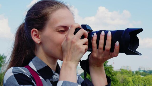 Positive girl takes pictures of sightseeing attractions while travelling in strange city. Young woman smiling, shooting urban landmarks. Photographer takes pictures. Close up