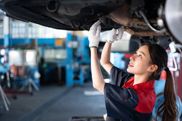 Selective focus of a young pretty Asian female mechanic in uniform, wearing work gloves examining...
