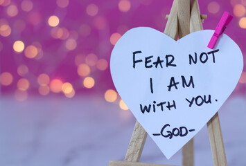 Fear not, I am with you, handwritten text verse on heart-shaped note with blurred bokeh background....