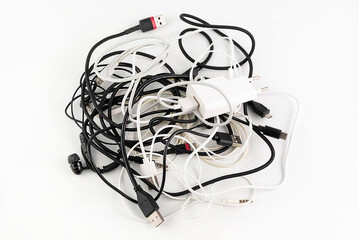 On a light background, a bunch of tangled wired headphones, chargers and wires.