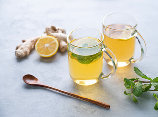 Two glasses of tea with fresh lemon, mint and ginger on a light background with morning light. The concept of a healthy drink for immunity.