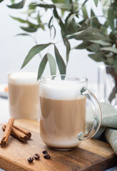 Two cappuccino or latte with milk foam in glasses on a wooden plate with coffee beans, cinnamon and...
