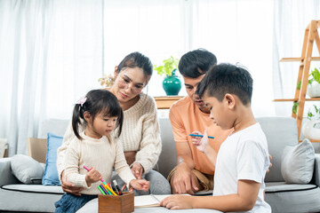 family love warmth. Asian parents are lounging on sofa in living room of house and their son and daughter drawing on coloring book with mom and dad guiding next to woman. Pregnancy, big belly.