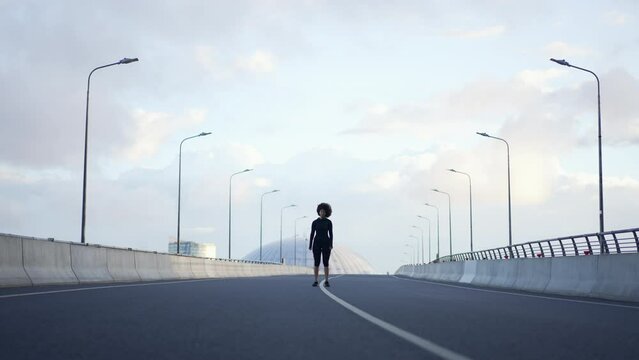 4k Sportswoman does cardio on bridge in city spbas. Young American African female doing fit exercise and jumping actively, getting ready to run and having good time outdoors. Attractive athletic lady