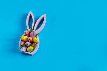 Wooden easter bunny figurine with spring tulips on the blue background, easter minimal concept, flat lay with copy space