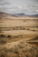 View of trail running through flat grassy valley with rolling desert bluffs in distance