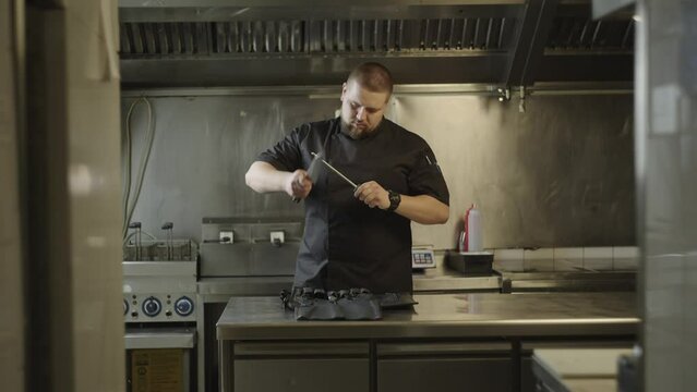 A chef sharpens a knife in a restaurant kitchen. A professional chef prepares to prepare dishes and sharpens a knife.