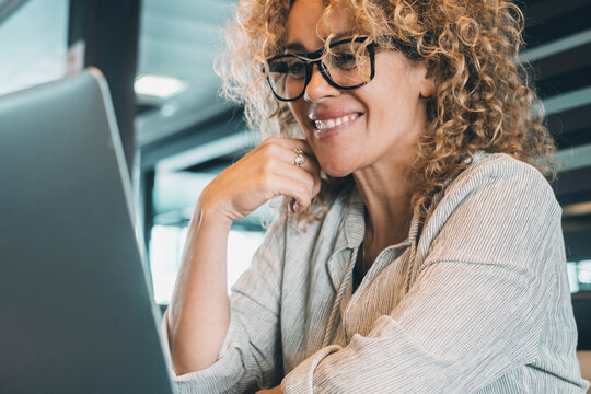 Portrait of cheerful young adult woman using latop at the office. Confident businesswoman with eyeglasses smile at the computer display. Video call conference online. Attractive entrepreneur cheerful