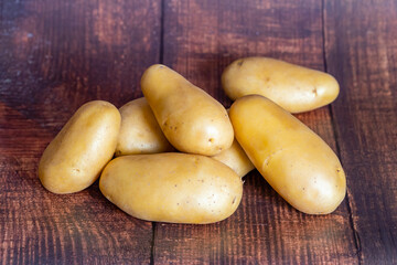 Heap of raw potatoes on brown rustic wooden table.
