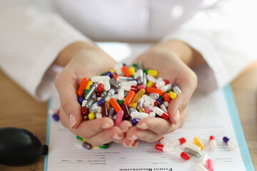 Female pharmacist shows bunch of different colorful pills while sitting at table.