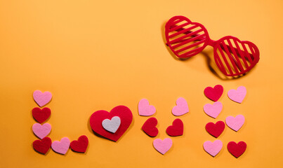 The concept of Valentine's Day. View from above. Red glasses are nearby. The inscription love is laid out on a yellow background of small pink and red hearts.