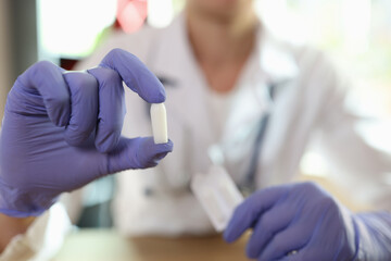Gynecologist in glove shows suppositories in her hand while sitting in medical clinic office.