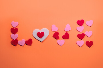 The inscription love is laid out on a soft pink background of small pink and red hearts. View from above. The concept of Valentine's Day.