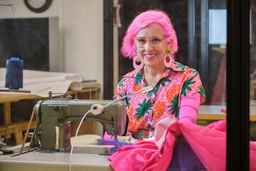 Tailor with pink hair and colorfull clothes smiling and looking at camera working on an industrial...