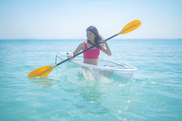 An Asian woman, a tourist, paddling a boat, canoe, kayak or surfboard with clear blue turquoise...