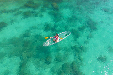 Fototapeta na wymiar Aerial top view of Asian woman, a tourist, paddling a boat, canoe, kayak or surfboard with clear blue turquoise seawater, Andaman sea in Phuket island in summer season, Thailand. Water in ocean