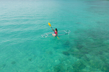 Aerial top view of Asian woman, a tourist, paddling a boat, canoe, kayak or surfboard with clear blue turquoise seawater, Andaman sea in Phuket island in summer season, Thailand. Water in ocean