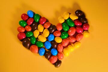 Concept of Valentine's Day. View from above. Flatlay greeting card. Colorful sweet candies are laid out in the shape of a heart. Yellow background.