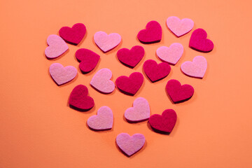 Small pink and red hearts on a soft background are laid out in the shape of a large heart. View from above. Flatlay greeting card. The concept of Valentine's Day.