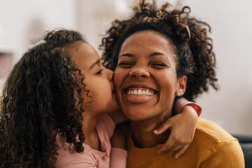 Cute mixed race girl is kissing her mother on the cheek - obrazy, fototapety, plakaty