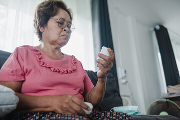 Asian senior woman reading medicine bottle label, home health care concept.