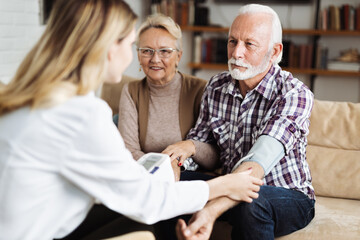 Obraz premium Female nurse checking blood pressure of a senior man during her home visit