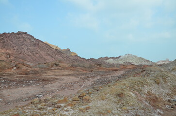 barren landscape with some low plants and beautiful colored mountains in background at Hormuz island, Iran