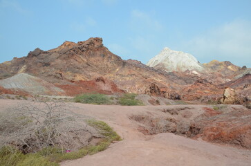 barren landscape with some low plants and beautiful colored mountains in background at Hormuz island, Iran